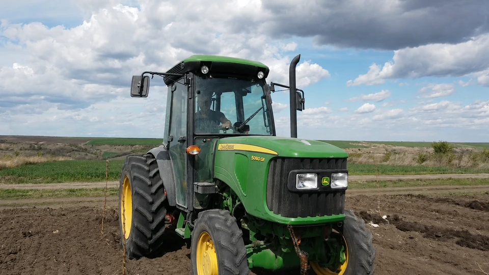 Tractorul verde al fermei oprit pe pământul arat dintre rândurile tinere de pomi.